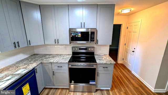 kitchen featuring decorative backsplash, light stone countertops, appliances with stainless steel finishes, and hardwood / wood-style flooring