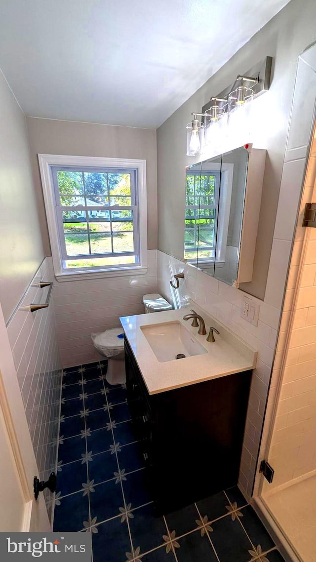 bathroom featuring toilet, vanity, a shower with door, and tile walls