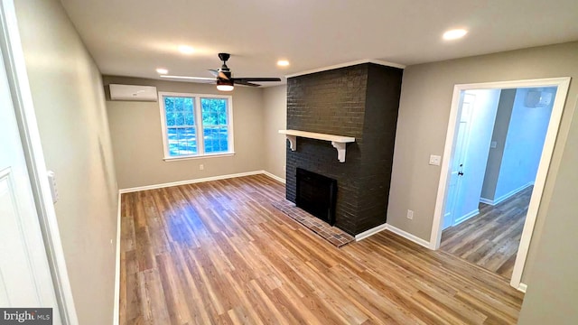 unfurnished living room featuring a brick fireplace, a wall unit AC, hardwood / wood-style flooring, and ceiling fan