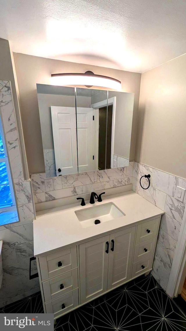 bathroom featuring a textured ceiling, vanity, and tile walls