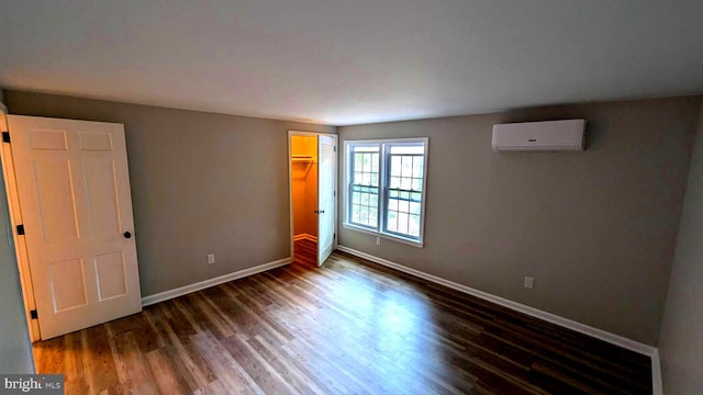 unfurnished bedroom with a closet, dark wood-type flooring, a spacious closet, and an AC wall unit