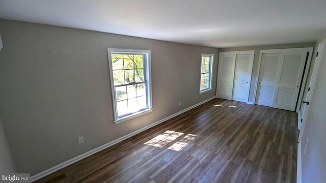 unfurnished bedroom with two closets, dark wood-type flooring, and multiple windows