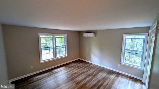 unfurnished room with a wall mounted air conditioner, dark hardwood / wood-style flooring, and a healthy amount of sunlight