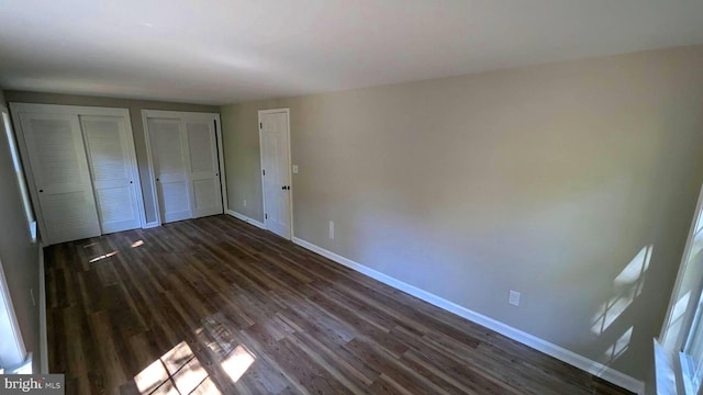 unfurnished bedroom with multiple closets and dark wood-type flooring