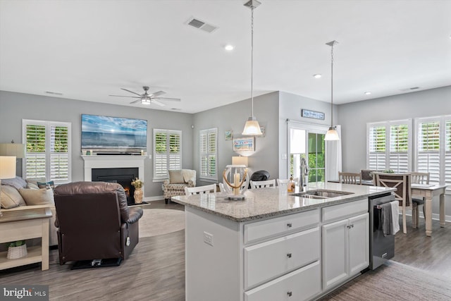 kitchen with white cabinetry, light stone counters, pendant lighting, a center island with sink, and sink