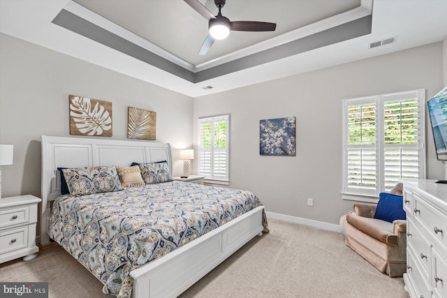 carpeted bedroom with ceiling fan, a raised ceiling, and multiple windows