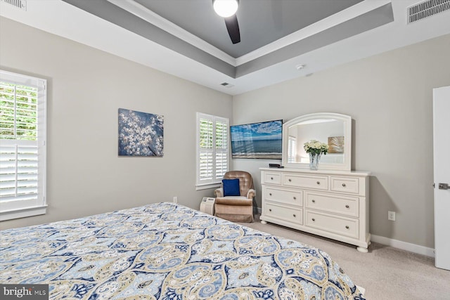 carpeted bedroom featuring ceiling fan, a tray ceiling, and multiple windows