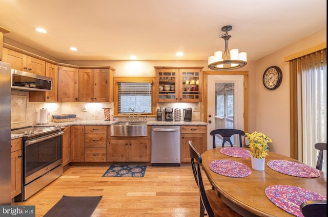 kitchen featuring light wood-type flooring, plenty of natural light, sink, appliances with stainless steel finishes, and decorative light fixtures