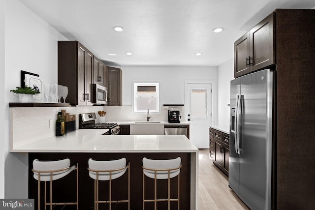 kitchen with sink, kitchen peninsula, light hardwood / wood-style flooring, appliances with stainless steel finishes, and a kitchen breakfast bar