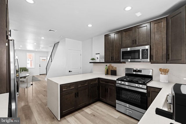 kitchen with kitchen peninsula, light hardwood / wood-style floors, appliances with stainless steel finishes, and dark brown cabinetry