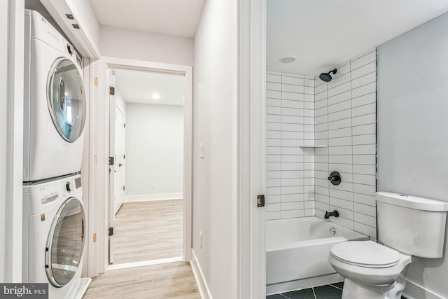 bathroom with hardwood / wood-style floors, tiled shower / bath combo, toilet, and stacked washing maching and dryer