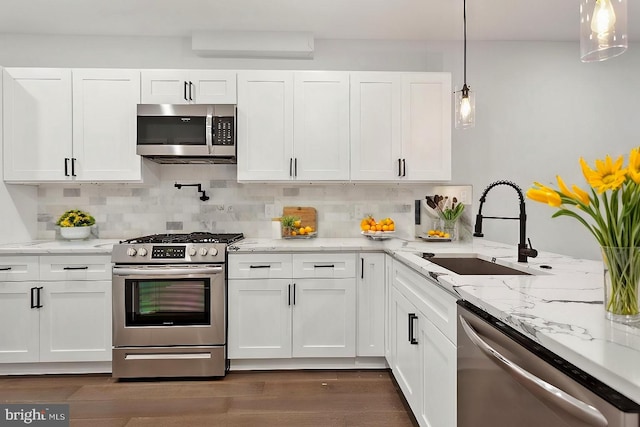 kitchen with decorative backsplash, appliances with stainless steel finishes, sink, white cabinets, and hanging light fixtures