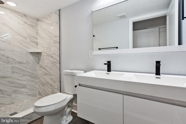 bathroom featuring vanity, toilet, and a tile shower