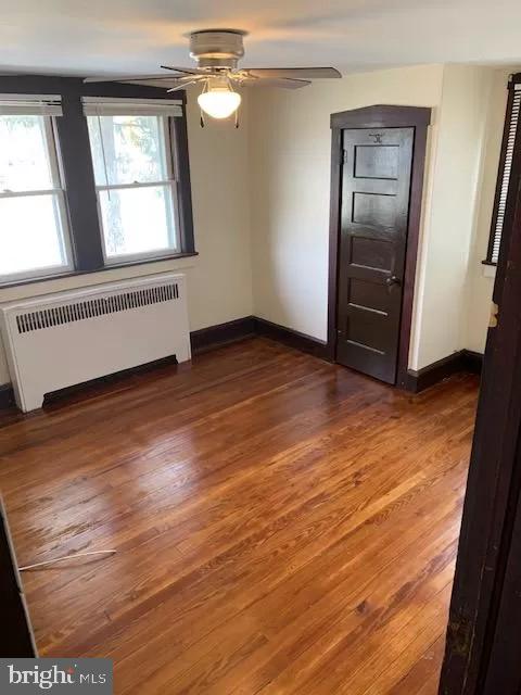 empty room with ceiling fan, radiator, and dark wood-type flooring