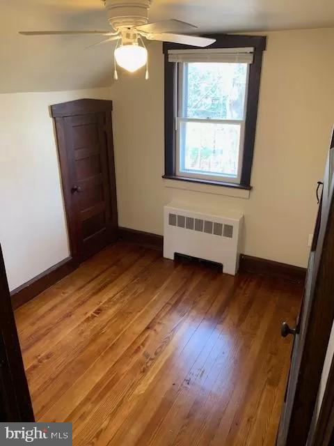 bonus room with wood-type flooring, ceiling fan, and radiator heating unit