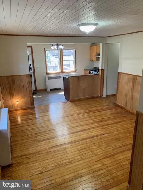 kitchen with wooden ceiling, wood walls, radiator heating unit, and light hardwood / wood-style flooring