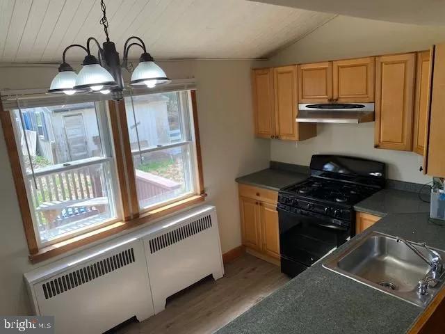 kitchen with a notable chandelier, lofted ceiling, black gas range oven, hanging light fixtures, and radiator heating unit