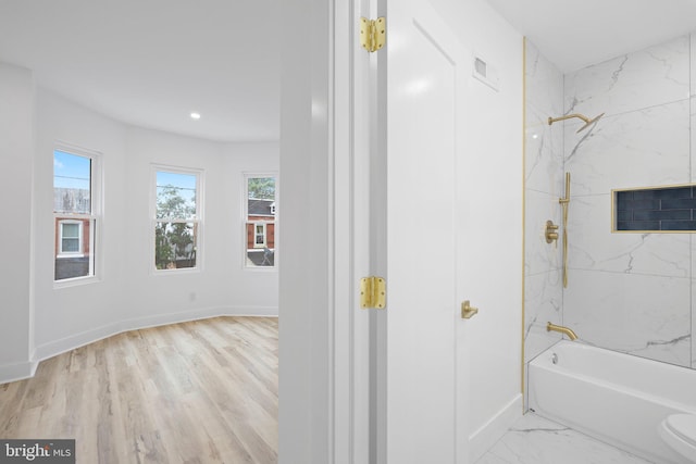 bathroom with wood-type flooring, toilet, and tiled shower / bath