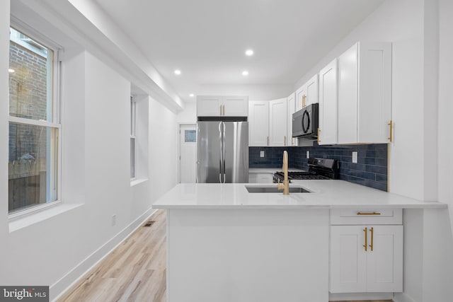 kitchen with light hardwood / wood-style flooring, white cabinets, black appliances, and kitchen peninsula