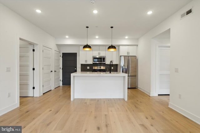 kitchen with appliances with stainless steel finishes, hanging light fixtures, light wood-type flooring, and an island with sink