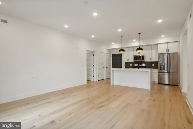 kitchen featuring light wood-type flooring, white cabinets, hanging light fixtures, a kitchen island, and stainless steel appliances