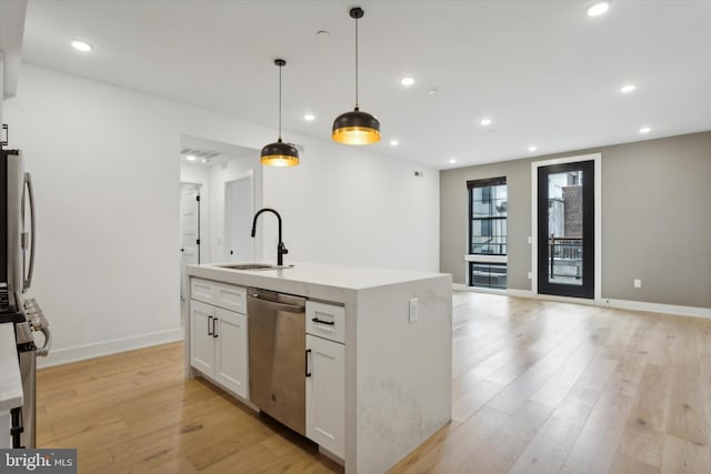 kitchen featuring white cabinetry, stainless steel appliances, decorative light fixtures, a kitchen island with sink, and sink