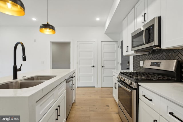 kitchen with pendant lighting, white cabinets, appliances with stainless steel finishes, and light wood-type flooring