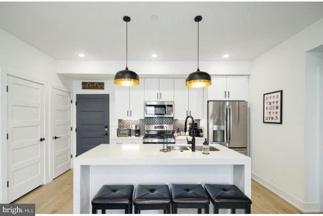 kitchen featuring white cabinets, an island with sink, appliances with stainless steel finishes, a breakfast bar area, and light wood-type flooring