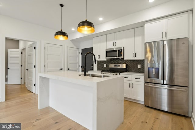 kitchen with sink, decorative light fixtures, a kitchen island with sink, appliances with stainless steel finishes, and light hardwood / wood-style floors