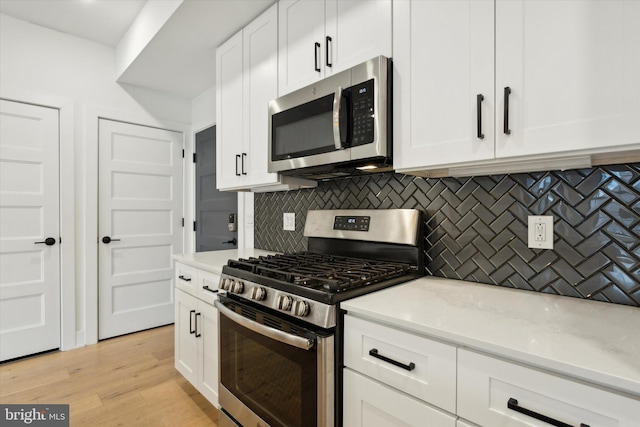 kitchen featuring white cabinets, stainless steel appliances, light stone countertops, light hardwood / wood-style floors, and decorative backsplash