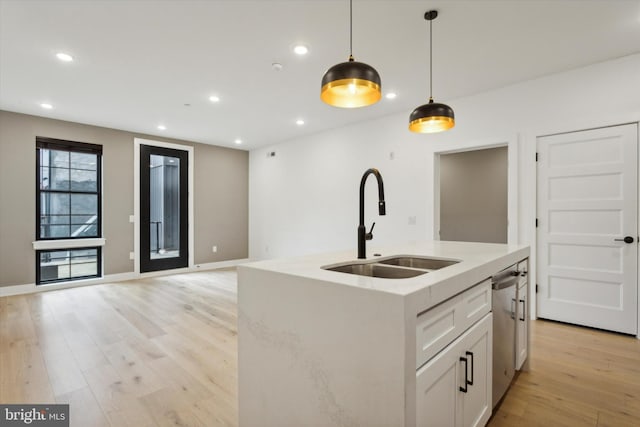 kitchen featuring sink, decorative light fixtures, a kitchen island with sink, white cabinetry, and light hardwood / wood-style floors