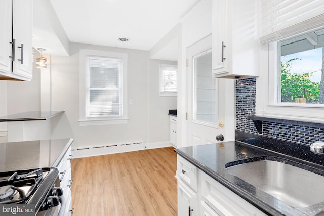 kitchen with light hardwood / wood-style floors, tasteful backsplash, gas stove, decorative light fixtures, and white cabinetry