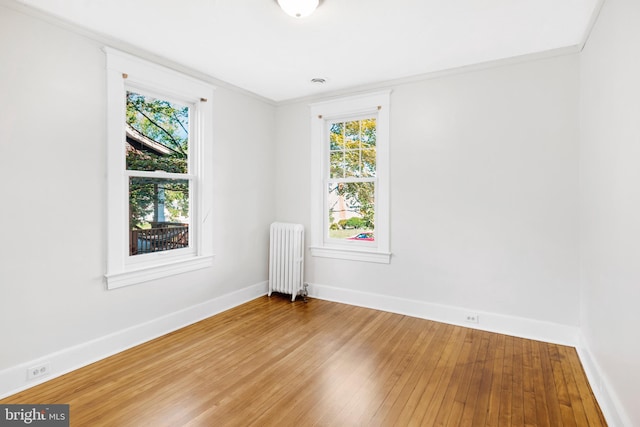 unfurnished room with radiator heating unit, ornamental molding, hardwood / wood-style flooring, and a wealth of natural light