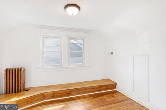 additional living space with hardwood / wood-style floors, lofted ceiling, and radiator heating unit