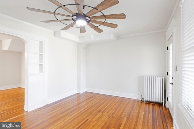 empty room with ornamental molding, ceiling fan, radiator heating unit, and wood-type flooring