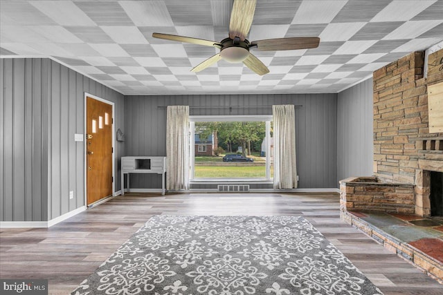 living room featuring ceiling fan, a fireplace, hardwood / wood-style flooring, and wood walls