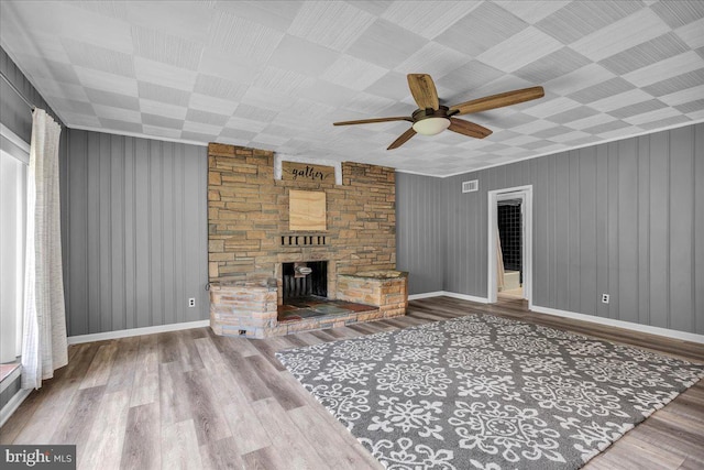 unfurnished living room with ceiling fan, wood walls, a fireplace, and hardwood / wood-style floors