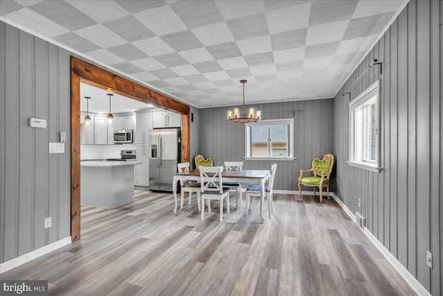 dining area with light hardwood / wood-style floors, a notable chandelier, and wooden walls