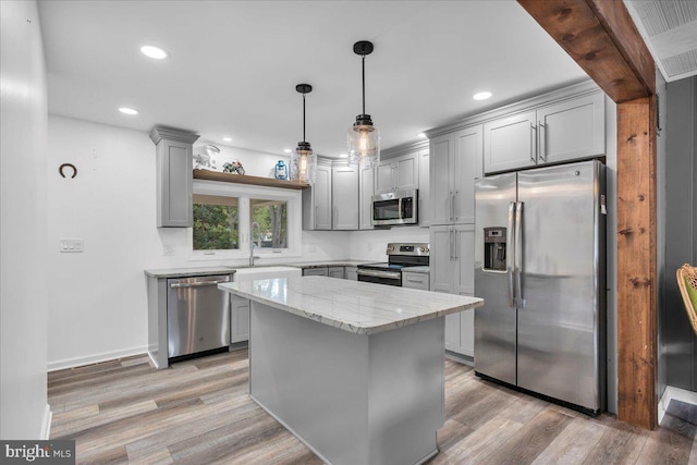 kitchen with gray cabinetry, decorative light fixtures, appliances with stainless steel finishes, light stone counters, and light hardwood / wood-style floors