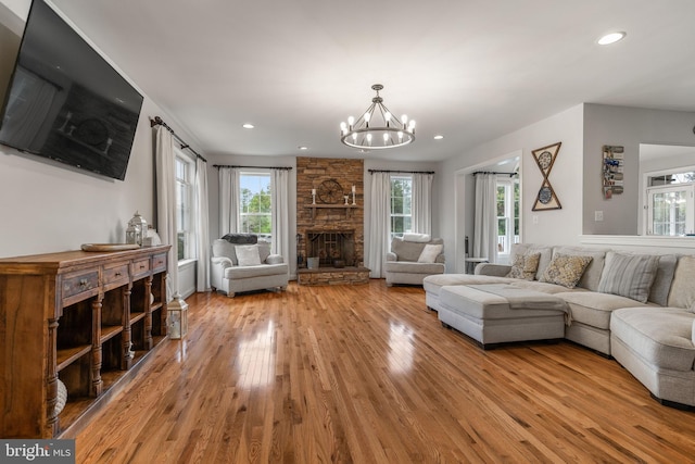 living room with light wood-type flooring, a stone fireplace, and a chandelier