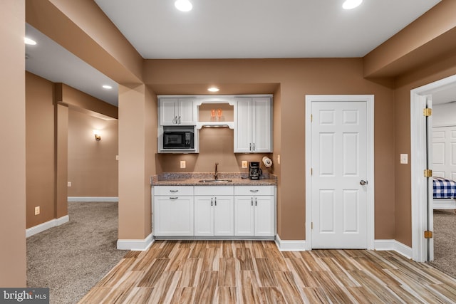 kitchen featuring white cabinetry, black microwave, dark stone counters, sink, and light colored carpet