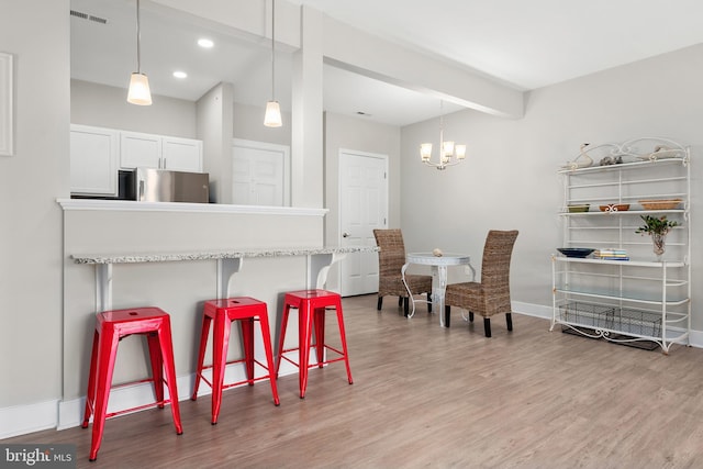 kitchen with white cabinets, stainless steel fridge, a kitchen breakfast bar, light hardwood / wood-style floors, and decorative light fixtures