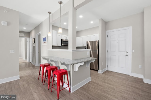 kitchen with a breakfast bar area, stainless steel appliances, decorative light fixtures, white cabinetry, and light hardwood / wood-style floors