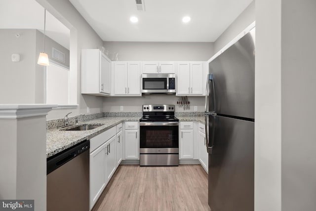 kitchen with sink, light wood-type flooring, stainless steel appliances, decorative light fixtures, and white cabinets