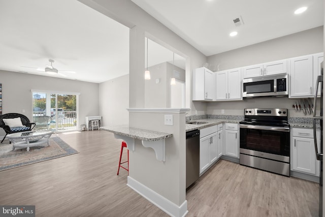 kitchen with white cabinets, stainless steel appliances, light hardwood / wood-style flooring, and a kitchen breakfast bar