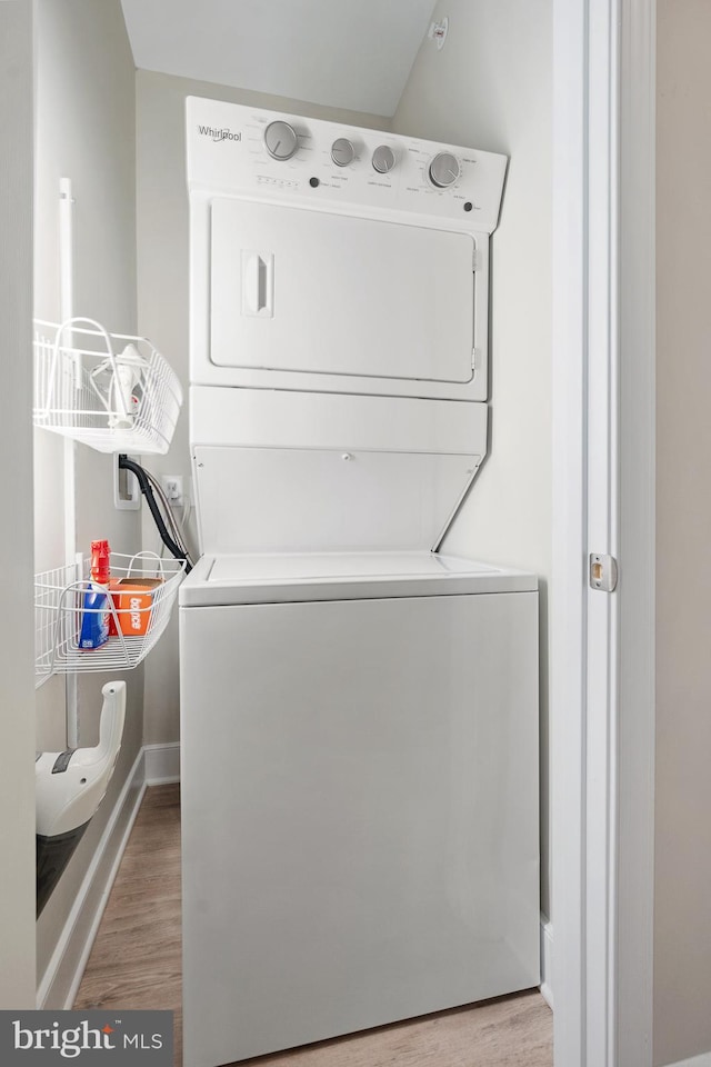 clothes washing area featuring hardwood / wood-style flooring and stacked washer and clothes dryer