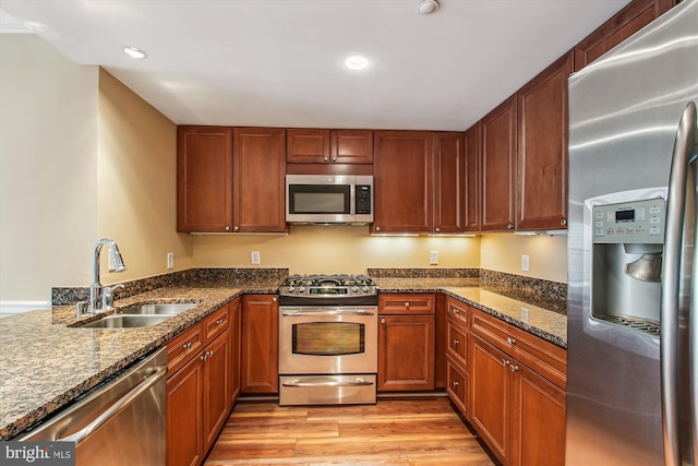 kitchen featuring sink, kitchen peninsula, light hardwood / wood-style flooring, appliances with stainless steel finishes, and dark stone countertops