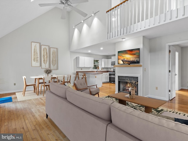 living room with light hardwood / wood-style flooring, high vaulted ceiling, sink, and ceiling fan