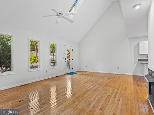 unfurnished living room with ceiling fan, high vaulted ceiling, a skylight, and light hardwood / wood-style flooring