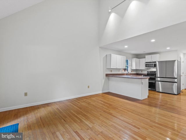 kitchen with light wood-type flooring, appliances with stainless steel finishes, kitchen peninsula, and white cabinets